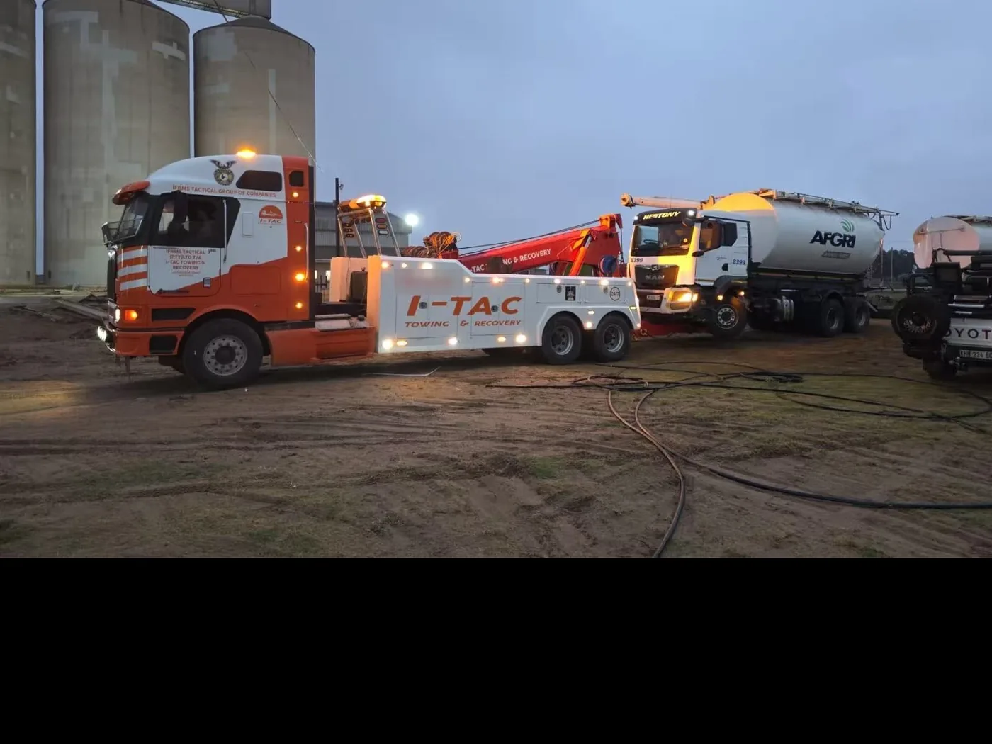 Integrated wrecker recovering a tanker truck at night